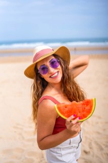 Caucasian woman enjoying summer on the beach on vacation with hat and a watermelon