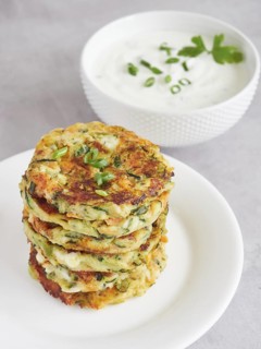 Stack of crispy and appetizing vegetable pancakes on a plate with yogurt and herb sauce dressing.