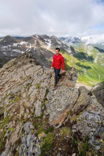 Mountaineer on a steep rocky ridge, on the summit of the Lasörling, view of the mountain panorama