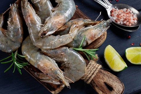 Fresh raw, white-footed shrimp, tiger prawns vannamei, on a wooden cutting board, with lime slices,