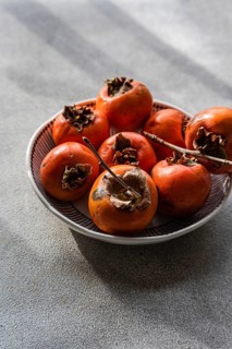 Bowl of fresh, ripe persimmons freshly picked from the orchard, showcased on a subtly textured gray