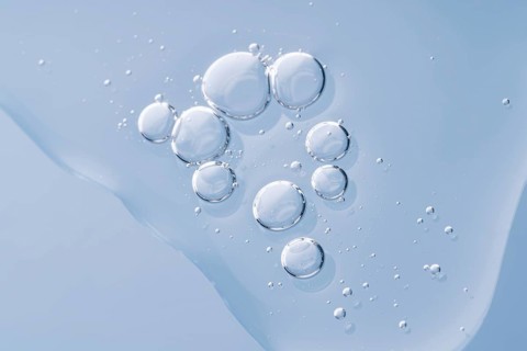 Clear, glistening serum drops elegantly arranged on a smooth, blue surface, reflecting purity and