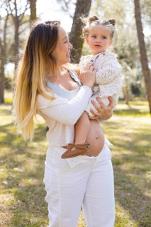 A joyful maternity scene outdoors, featuring a pregnant mother holding her young child. Sunlight