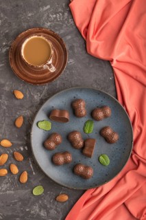 Chocolate candies with almonds and a cup of coffee on a black concrete background and red textile.