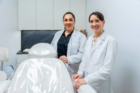 Two female doctors in lab coats standing and smiling in a modern aesthetic clinic or medical spa,