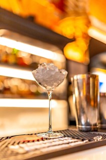 Vertical photo with no people of a luxury cocktail on a night club counter next to a shaker