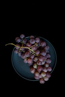 Red grape vine (Vitis vinifera) on plate against dark background