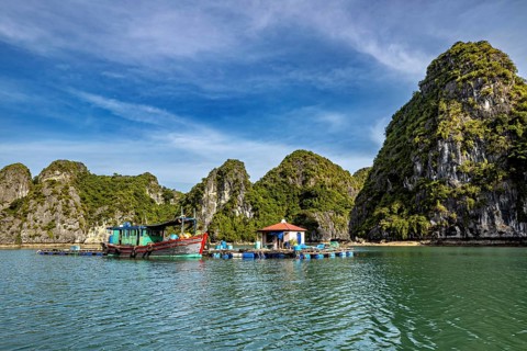 Small boat near houseboats and limestone rocks on calm waters, The floating villages in Halong Bay