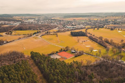 Extensive landscape with fields and forest, bordered by a village in the background, under cloudy