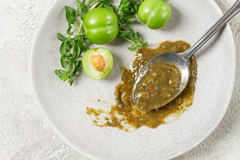 A spoon with tkemali sauce, on a plate, with cherry plum and mint, top view, no people