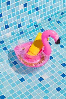 A vibrant yellow sunscreen bottle rests in a playful pink flamingo float on a pool's blue and white