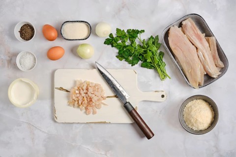 Various ingredients are arranged on a kitchen counter. There are fish fillets, herbs, eggs, and
