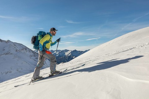 A man ski touring uphill on a pristine snowy mountain, equipped with poles and a backpack under a