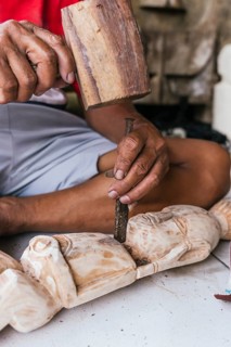 An Indonesian man skillfully carves a wooden sculpture using a chisel and mallet, showcasing