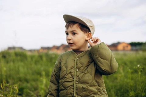 A young boy in a green jacket and cap walks through a lush green field, exploring the serene