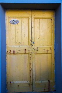 Close-up of yellow painted wood plank entrance doors on blue stucco cladded residential building
