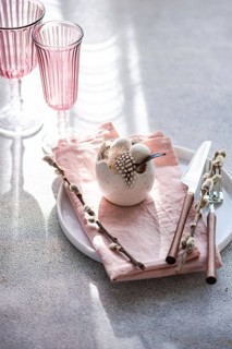 An elegant and festive Easter table setting in soft pastel hues. The focus is a decorative egg