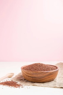 Wooden bowl with raw red quinoa seeds on a white and pink background and linen textile. Side view,