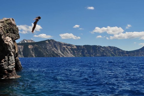 A person jumps from a rocky outcrop into the ice-cold, blue water of Crater Lake, Crater Lake