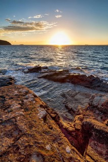 Sunset at the sea, rocky coast, container ships on the horizon, backlight, Little Haven,