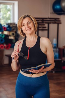 A woman personal trainer stands in a gym, smiling looking at camera while reviewing her planner.