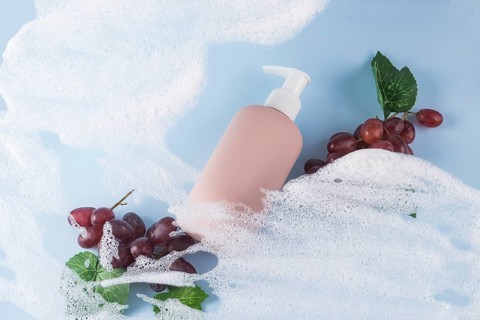 A pink bottle of grape-scented shower gel on a blue background. Surrounded by soap bubbles and red