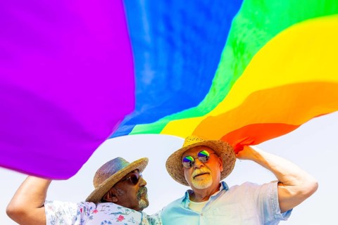 From below elderly gay couple, both men, enjoys a sunny day outdoors while holding a vibrant