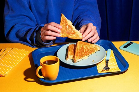 Overhead view of a person in a blue sweatshirt holding a crispy grilled cheese sandwich. Harsh