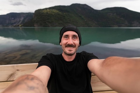 A cheerful traveler takes a selfie while sitting by a tranquil lake in Norway The calm turquoise
