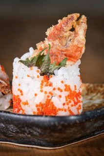 Gunkan maki sushi topped with fried soft shell crab, tobiko and shiso leaf, served on a black plate