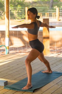 Young woman practicing virabhadrasana ii yoga pose on a mat outdoors, showcasing balance and