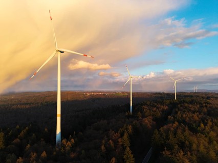 Wind turbines stand high above treetops as clouds gather in the sky, wind turbine, near