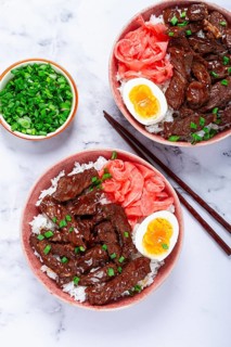 Gyudon Japanese beef with rice, pickled ginger, boiled egg slice, garnished with green onions, in a