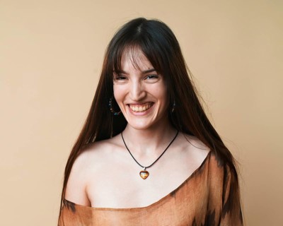 Portrait of a joyful young woman wearing a brown patterned blouse and a necklace, laughing against