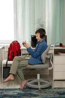 A young boy sits barefoot, focused on his mobile game. Wearing headphones, he enjoys gaming in his