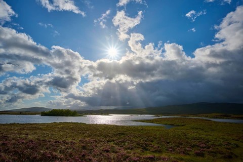 Sun shines behind clouds over river in a wide natural landscape, Rannoch Moor, Bridge of Orchy,