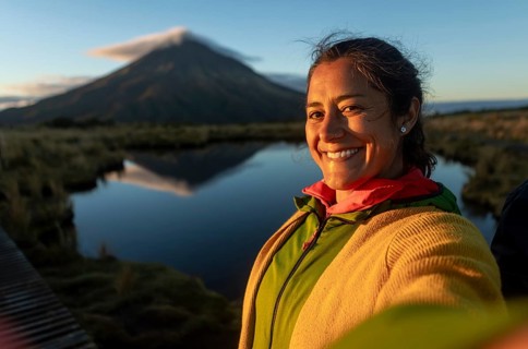 Smiling woman takes a selfie with scenic Mount Taranaki in the background, perfectly mirrored in a
