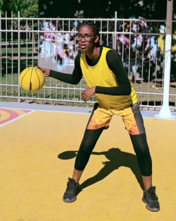 A woman athlete in sporty attire practices basketball on a vibrant outdoor court. Wearing a bright