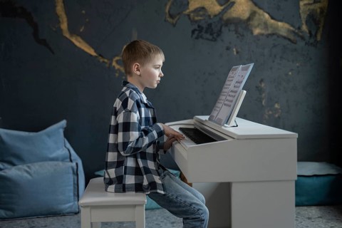 A young boy, focused and attentive, plays the piano while reading sheet music. Set in a cozy room
