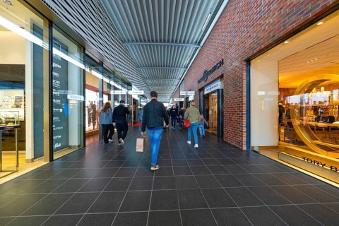 People walking inside a modern, brightly lit shopping centre, Outlet City Metzingen, Germany