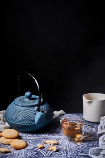 A cozy tea time setup featuring a blue teapot, a steaming cup of tea, and delicious cookies on a