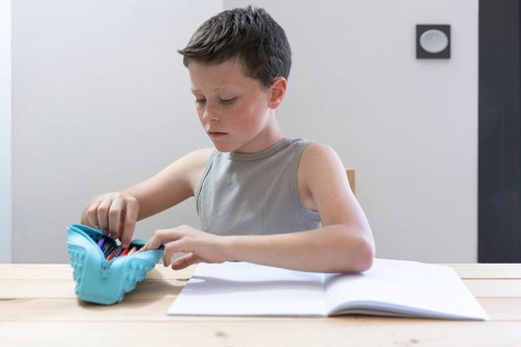 A focused young boy in a sleeveless shirt organizes colorful pencils from a turquoise case on a
