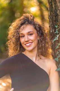Vertical photo of a smiling woman looking at camera standing in the forest