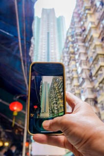 Cropped unrecognizable hand holding a smartphone capturing Hong Kong's towering buildings,