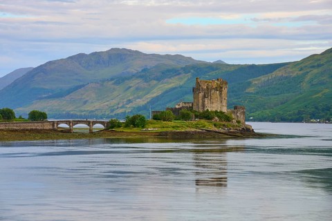 An old castle stands majestically on an island surrounded by water and green mountains under a