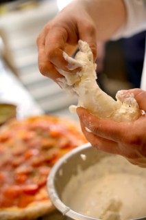 Cropped unrecognizable person preparing pizza dough with visible raw ingredients and tools in a