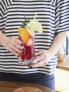 Refreshing cold red citrus drink with fresh lime, orange and lemon slices in glass in the hands of