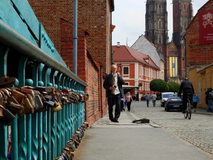 Scenic city view with cathedral bridge and love locks, musician with saxophone on sidewalk next to