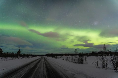 Vibrant Aurora Borealis lights up the night sky over a snow-covered road in Kiruna, Sweden,