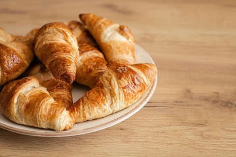 A plate of freshly baked homemade croissants sits invitingly on a wooden table. The golden, flaky